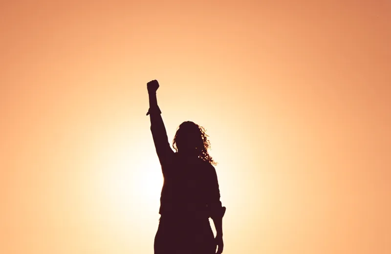 A person standing with arms raised at sunrise